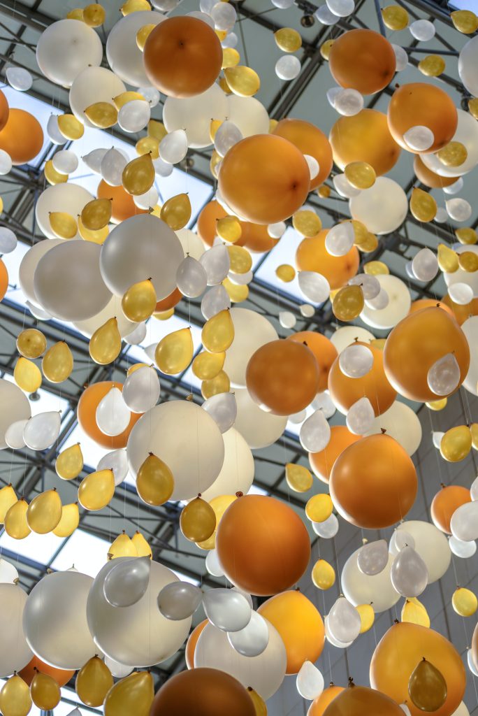 Gold, bronze, silver, and white Balloons hanging from a ceiling.
